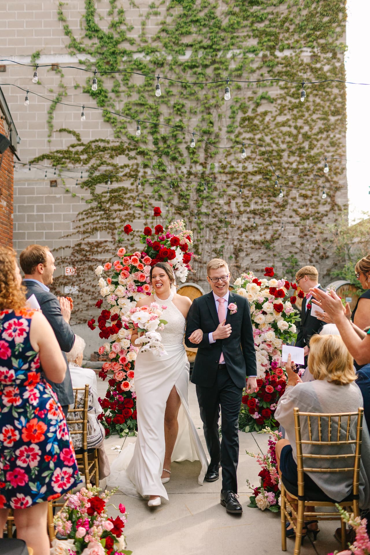 Newlyweds walking up the aisle between rose arrangements on the ivy-covered courtyard